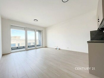 Světlý obývací pokoj s moderní parketovou podlahou, velká okna vedoucí na balkon, novostavba v minimalistickém stylu.
