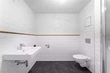 Moderní koupelna s bílými obklady, závěsnou toaletou a umyvadlem. Kombinace dlažby na podlaze a čistý design vytváří světlý prostor.