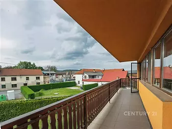 Prostorný balkon s dlažbou, dřevěným zábradlím a výhledem na okolní střechy. Vhodný pro relaxaci a sledování krajiny.