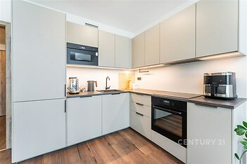 Moderní kuchyň s vestavěnými spotřebiči, parketová podlaha, světlé skříňky a dřevěné detaily, elegantní a funkční design.