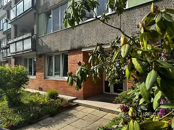 Vstup do bytového domu s cihlovým obkladem, moderní fasádou a okny s dvojitým sklem. Zeleň v okolí vytváří příjemné prostředí.