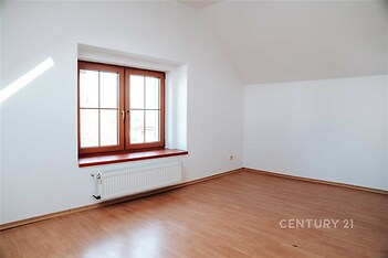 Prostorná ložnice s laminátovou podlahou, velké okno s dřevěným rámem zajišťuje světlo, čisté bílé stěny poskytují moderní vzhled.