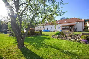 Prostorná zahrada s pečlivě udržovaným trávníkem, venkovní terasa, vzrostlé stromy, klidné okolí vhodné pro relaxaci.