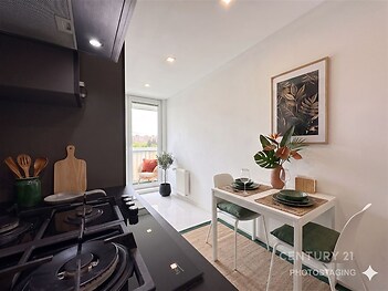 Moderní kuchyň s keramickou dlažbou, elegantní černou pracovní deskou a vestavěnými spotřebiči. Je propojena s jídelním koutem a má přístup na balkon.