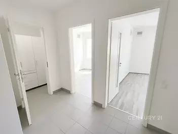 Světlá chodba s dlažbou, která vede do dvou pokojů. Moderní povrchové úpravy a čisté bílé zdi vytvářejí prostorný dojem.