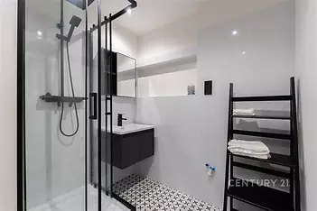 Moderní koupelna s proskleným sprchovým koutem, bílými dlaždicemi a dlažbou s geometrickým vzorem, elegantní černé prvky dodávají styl.