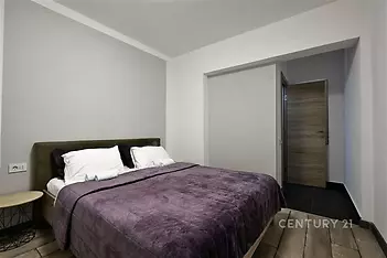 Prostorná ložnice s dřevěnou podlahou, moderní design a přírodní tóny, vybavená pohodlnou postelí a velkými polštáři.