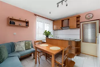 Kuchyňský kout s moderní dřevěnou linkou a světlou dlažbou, vedle jídelního stolu se nachází pohodlná sedací souprava, velké okno zajišťuje dostatek světla.