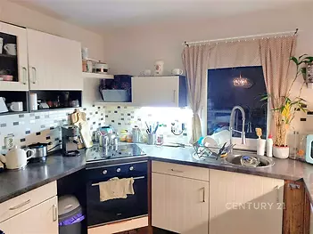 Moderní kuchyň s dlažbou a vestavěnými spotřebiči. Velká okna s elegantními závěsy zajišťují světlost prostoru.