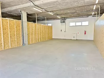 Průmyslový skladový prostor s betonovou podlahou, OSB přepážkami a vysokými stropy, ideální pro skladování či dílenské využití.