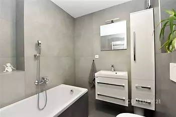 Moderní koupelna s dlažbou, bílými skříňkami a zrcadlem nad umyvadlem, nabízí elegantní a funkční interiér pro pohodlné bydlení.