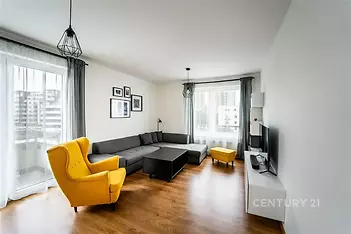Světlý obývací pokoj s parketovou podlahou, velká okna, moderní design, pohodlná sedací souprava, žluté křeslo pro kontrast.