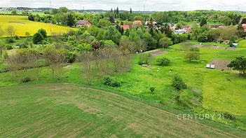 Rozlehlý stavební pozemek s travnatým porostem, obklopený zelení a blízkostí rodinných domů, ideální pro klidnou rezidenční výstavbu.