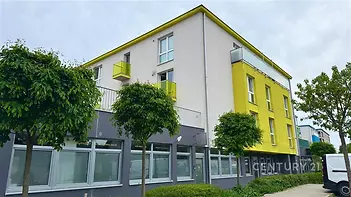 Moderní bytový dům s barevnou fasádou, plastovými okny a zelenými balkony, vhodný pro rodinné bydlení ve městě.