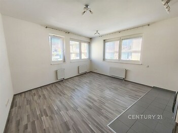 Světlý obývací pokoj s moderními podlahami, velká okna poskytují dostatek přirozeného světla, stěny v neutrálních tónech, ideální pro osobní úpravy.