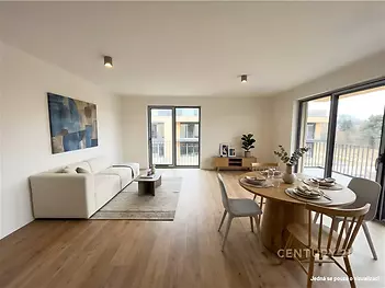 Světlý obývací pokoj s moderní parketovou podlahou, velká okna a elegantní nábytek, ideální pro prostorné rodinné bydlení.