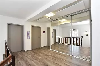 Chodba s laminátovou podlahou, vestavěné skříně a moderní design, světlý prostor díky velkým oknům a minimalistické osvětlení.