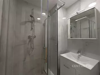 Moderní koupelna s proskleným sprchovým koutem, světlými dlažbami a elegantním umyvadlem, ideální pro moderní bydlení.