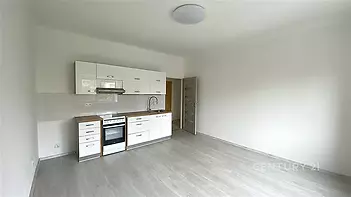 Moderní kuchyň s bílými skříňkami, vestavěnou troubou a laminátovou podlahou, světlý interiér, jednoduchý design