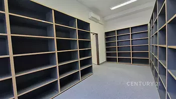 Prostorná kancelář s vestavěnými policemi, světlý interiér s moderní klimatizací a kobercovou podlahou, ideální pro organizaci a skladování.