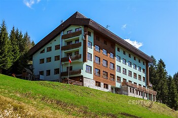 Horská chata s dřevěným obkladem, velkými okny a moderní fasádou se nachází uprostřed lesů na svahu, vytváří klidnou rekreační atmosféru.