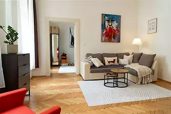 Světlý obývací pokoj s parketovou podlahou, moderním designem, velkými okny a pohodlnou sedací soupravou.