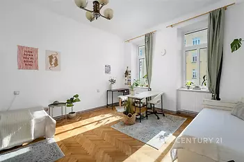 Světlý obývací pokoj s parketovou podlahou, velká okna poskytují dostatek přirozeného světla, moderní dekorace a výhled do ulice