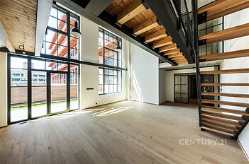 Světlý obývací pokoj s velkými okny, dřevěnými stropy a moderním schodištěm, parketová podlaha, industriální styl, dvojpodlažní prostor.