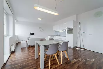 Moderní obývací pokoj s kuchyňským koutem, parketová podlaha, bílá kuchyňská linka, světlý interiér, velká okna pro více světla.