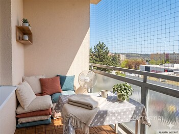 Prostorný balkon s dřevěnou podlahou, výhledem na město a bezpečnostní sítí, ideální pro relaxaci nebo venkovní posezení