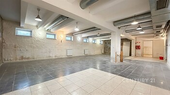 Průmyslový sklepní prostor s dlažbou, vysokými stropy a industriálními prvky, ideální pro komerční využití nebo úložné prostory.