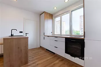 Moderní kuchyň s parketovou podlahou, vestavěnou troubou a velkými okny, nabízející světlý a vzdušný prostor.