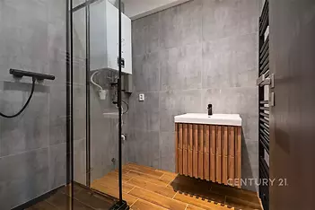 Moderní koupelna s dlažbou, proskleným sprchovým koutem a elegantní dřevěnou skříňkou. Tmavé dlaždice zvyšují stylový vzhled.
