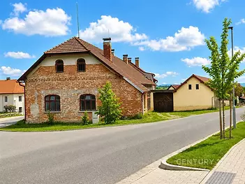 Cihlový dům s tradiční střešní krytinou na klidné ulici, obklopený zelení, nabízí potenciál pro rekonstrukci a modernizaci.