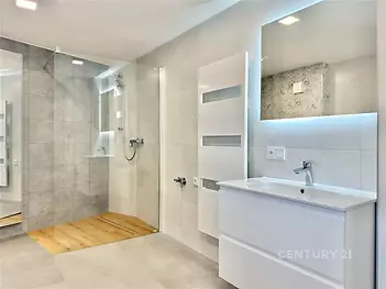 Prostorná koupelna s moderním designem, velká sprcha, keramická dlažba, světlé obklady, elegantní umyvadlo se zrcadlem