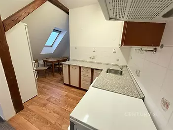 Malá kuchyň s dřevěnou podlahou, šikmým stropem a střešním oknem. Moderní vybavení a bílé obklady dodávají světlý vzhled.