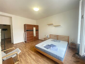 Prostorná ložnice s parketovou podlahou, dřevěnou postelí a vestavěnou skříní, moderní styl, světlý interiér s velkými okny.