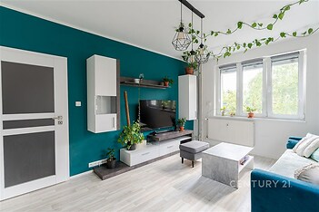 Světlý obývací pokoj s moderními prvky, parketovou podlahou, velká okna a minimalistický design, zdobený rostlinami a stylovým nábytkem.