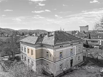 Historický dvoupatrový dům s šikmou střechou a omítkou, nachází se v klidné venkovské oblasti s panoramatickým výhledem na krajinu.