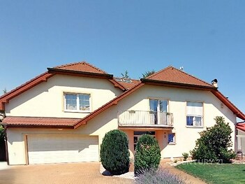 Velký rodinný dům s balkonem, červenou střechou a upravenou zahradou, nabízí klidné bydlení na okraji města.