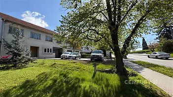 Řadový dům s červenou střechou v klidné lokalitě, předzahrádka se vzrostlým stromem, zpevněná příjezdová cesta, parkovací místa před domem.