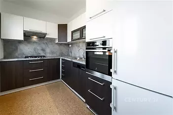 Moderní kuchyň s tmavou dřevěnou linkou, vestavěnými spotřebiči a světlou dlažbou vytváří elegantní a praktický prostor pro vaření.