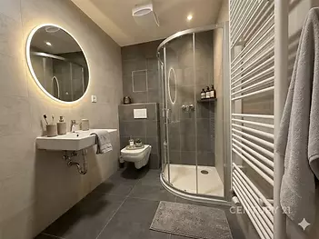 Moderní koupelna s velkoformátovými dlaždicemi, sprchovým koutem a kruhovým zrcadlem, která působí elegantně a svěže.