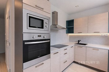 Moderní kuchyň s vestavěnými spotřebiči, světlými skříňkami a dlažbou. Nabízí elegantní úložné prostory a moderní design.