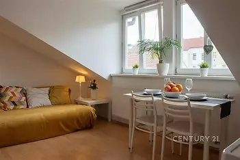 Podkrovní obývací pokoj s parketovou podlahou, velká okna propouštějící světlo, moderní nábytek a útulná atmosféra