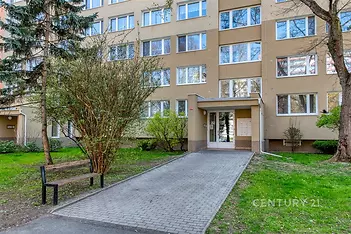 Vstup do bytového domu s rekonstruovanou fasádou, velkými okny a udržovanou zahradou.