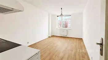 Světlá kuchyň s parketovou podlahou, velkým oknem a moderním designem nabízí prostor pro jídelní kout.