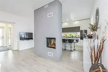 Moderní obývací pokoj s krbovými kamny, parketovou podlahou a světlým interiérem, propojený s kuchyní s moderními spotřebiči.