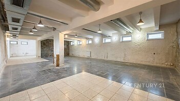Prostorný suterén s dlažbou, vysoké stropy a velká okna, industriální styl s viditelnými potrubími, vhodný pro komerční prostory