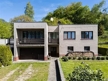 Rodinný dům s plochou střechou, betonovou fasádou a prostorným balkonem, obklopený zelení, ideální pro rodinné bydlení na klidném místě.